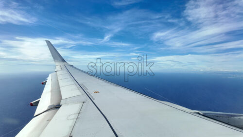 Aircraft wing glides above layered clouds and shimmering sea - Starpik Stock
