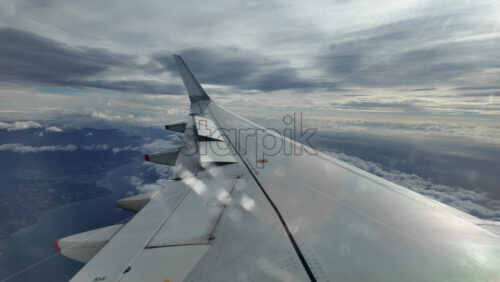 Aircraft wing gliding above layered clouds viewed from the window seat - Starpik Stock