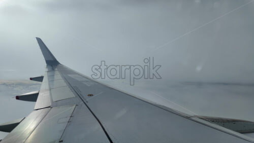 Aircraft wing gliding above layered clouds viewed from the window seat - Starpik Stock