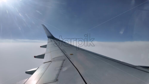 Aircraft wing gliding above layered clouds viewed from the window seat - Starpik Stock