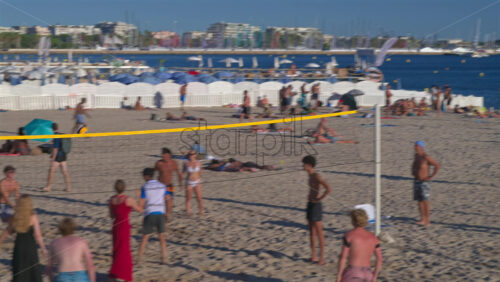 Antibes, France – June 15, 2025: People relaxing and having fun at the beach with boats docked on the Mediterranean sea on the background - Starpik Stock