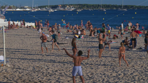 Antibes, France – June 15, 2025: People relaxing and having fun at the beach with boats docked on the Mediterranean sea on the background - Starpik Stock