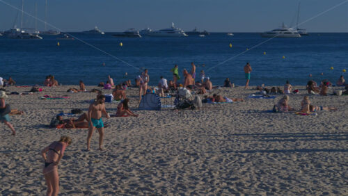 Antibes, France – June 15, 2025: People relaxing and having fun at the beach with boats docked on the Mediterranean sea on the background - Starpik Stock