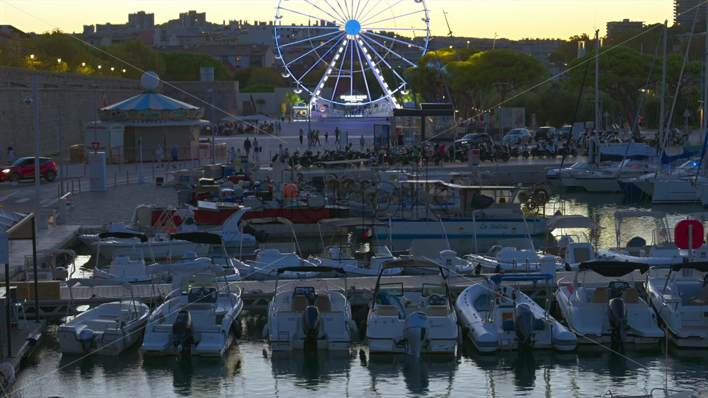 Antibes, France – June 7, 2025: Multiple white boats docked in the Port Vauban with the illuminated ferris wheel on the background in the evening - Starpik Stock
