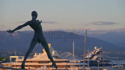 Antibes, France – June 8, 2025: Bronze sculpture “Grand Defi” by Nicolas Lavarenne with boats docked in the background - Starpik Stock