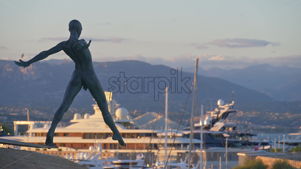Antibes, France – June 8, 2025: Bronze sculpture “Grand Defi” by Nicolas Lavarenne with boats docked in the background - Starpik Stock