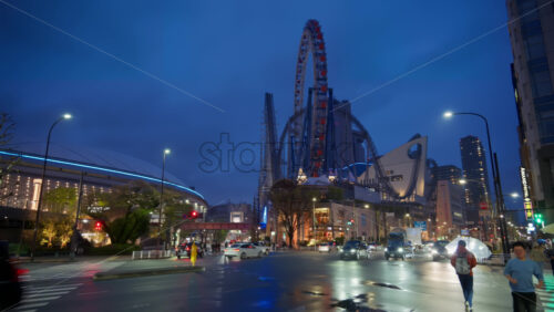 Bunkyo, Japan – April 13, 2025: Cars moving on the streets of the city with the Tokyo Dome City Attractions at the Amusement park on the background in the evening - Starpik Stock