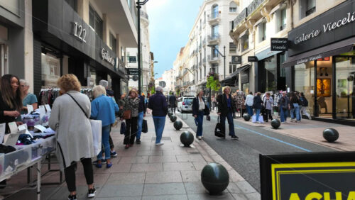 Cannes, France – August 4 2025: People walking on a shopping street with clothing racks lining the street and people browsing garments - Starpik Stock