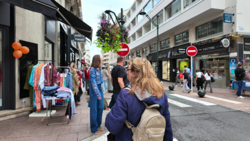 Cannes, France – August 4 2025: People walking on a shopping street with clothing racks lining the street and people browsing garments - Starpik Stock