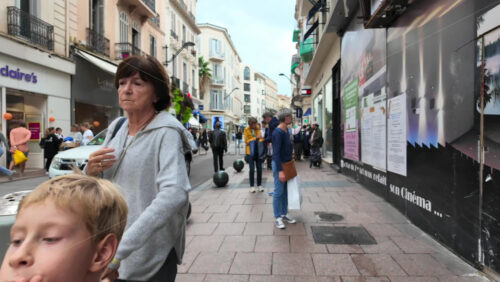 Cannes, France – August 4 2025: People walking on a shopping street with clothing racks lining the street and people browsing garments - Starpik Stock