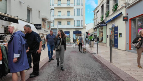 Cannes, France – August 4 2025: People walking on a shopping street with clothing racks lining the street and people browsing garments - Starpik Stock