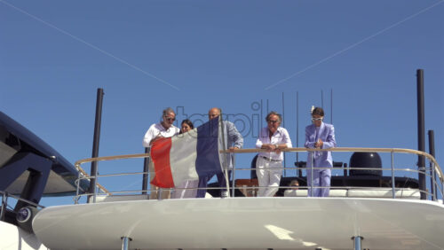 Cannes, France – July 10, 2025: People in smart attire leaning on the aft rail of a yacht under clear blue sky with the French flag waving at the stern - Starpik Stock