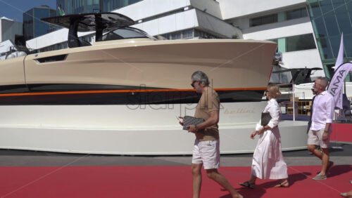 Cannes, France – July 10, 2025: People walking along a red carpet in front of a large beige-and-black boat through the Cannes Port in daylight - Starpik Stock