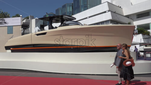 Cannes, France – July 10, 2025: People walking along a red carpet in front of a large beige-and-black boat through the Cannes Port in daylight - Starpik Stock