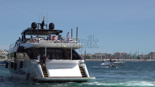 Cannes, France – July 10, 2025: Woman in a blue suit leaning on the aft rail of a yacht under clear blue sky with the French flag waving at the stern - Starpik Stock