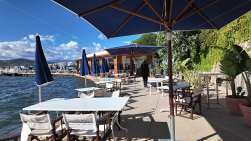 Cannes, France – July 12, 2025: A peaceful seaside walkway lined with terracotta pots, banana leaves and umbrellas overlooking blue water - Starpik Stock