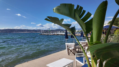 Cannes, France – July 12, 2025: A peaceful seaside walkway lined with terracotta pots, banana leaves and umbrellas overlooking blue water - Starpik Stock