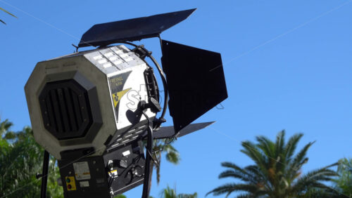 Cannes, France – July 2, 2025: Close up of a professional Fresnel 4 kW studio light against a bright blue sky, with tropical palm trees in the background - Starpik Stock