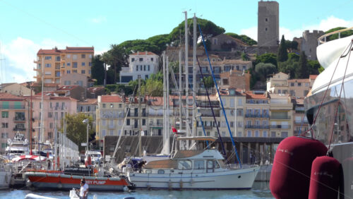 Cannes, France – July 2, 2025: Distant view from the Old Port of the flag of France waving on top of the Museum of World Explorations near green trees - Starpik Stock