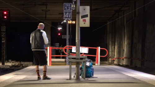 Cannes, France – July 2, 2025: Man standing on an underground train platform with a backpack and drink beside him, as a train approaches in the tunnel - Starpik Stock
