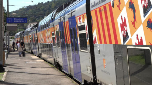 Cannes, France – July 2, 2025: Passengers with luggage boarding the train at a station with a sign indicating the direction to Marseille in the background - Starpik Stock