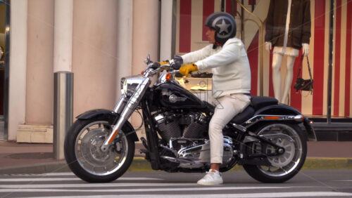 Cannes, France – July 6, 2025: Man in white clothing and helmet sitting on a Harley-Davidson motorcycle at a pedestrian crossing in the city centre - Starpik Stock