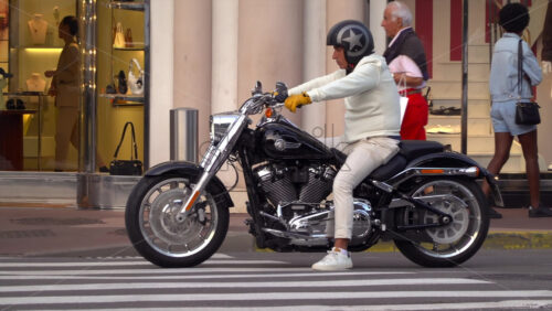 Cannes, France – July 6, 2025: Man in white clothing and helmet sitting on a Harley-Davidson motorcycle at a pedestrian crossing in the city centre - Starpik Stock