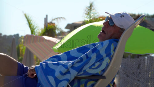 Cannes, France – July 9, 2025: Older man reclining on a beach chair with sunglasses, white cap, and patterned blue towel - Starpik Stock