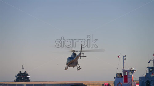 Cannes, France – June 22, 2025: A black helicopter flying low above a dock with boats moored nearby under bright daylight - Starpik Stock