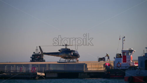 Cannes, France – June 22, 2025: A black helicopter flying low above a dock with boats moored nearby under bright daylight - Starpik Stock