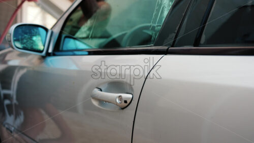 Chisinau, Moldova – August 18, 2025: A man washing a silver car window with a cleaning brush, removing soap and dirt - Starpik Stock