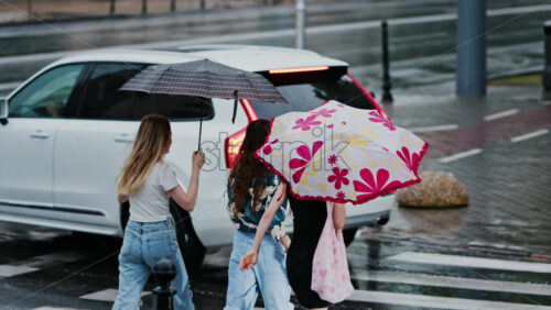 Chisinau, Moldova – June 11, 2025: Three girls crossing the street while holding umbrellas in the rain - Starpik Stock