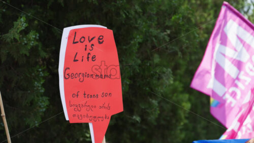 Chisinau, Moldova – June 15, 2025: Close up of hands holding a sign reading “Love is life. Georgian mama of trans son” at the Pride March in the city center - Starpik Stock
