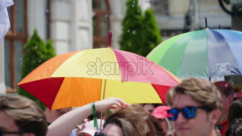 Chisinau, Moldova – June 15, 2025: People marching and holding rainbow umbrellas at the Pride Parade in the city center with small soap bubbles flying through the air - Starpik Stock