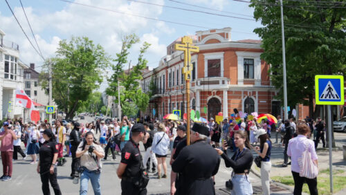 Chisinau, Moldova – June 15, 2025: Priest holding a big cross in front of policemen protecting the people marching and holding signs at the Pride Parade in the city center - Starpik Stock