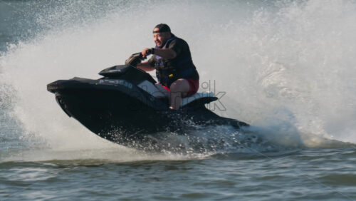 Chisinau, Moldova – June 17, 2025: A man in a black life vest riding a black jet ski at high speed across a calm body of water - Starpik Stock