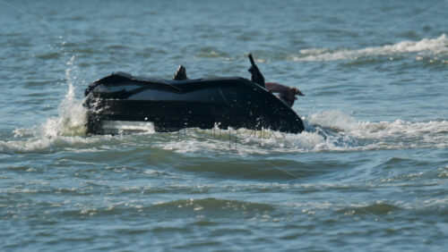 Chisinau, Moldova – June 17, 2025: A man in a black life vest riding a black jet ski at high speed across a calm body of water - Starpik Stock