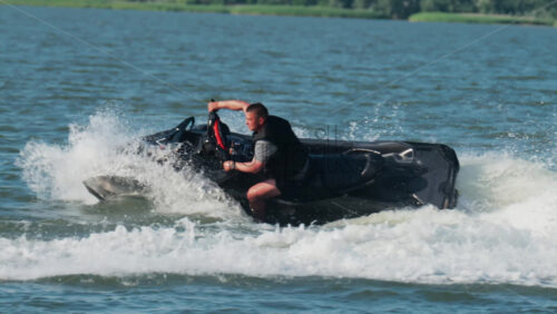 Chisinau, Moldova – June 17, 2025: A man in a black life vest riding a black jet ski at high speed across a calm body of water - Starpik Stock
