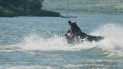 Chisinau, Moldova – June 17, 2025: A man in a black life vest riding a black jet ski at high speed across a calm body of water - Starpik Stock