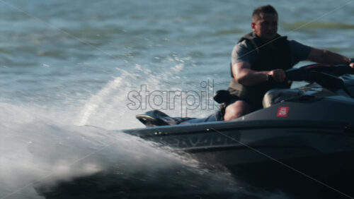 Chisinau, Moldova – June 17, 2025: A man in a black life vest riding a black jet ski at high speed across a calm body of water - Starpik Stock
