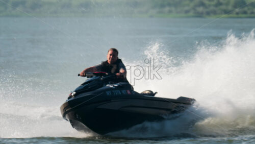 Chisinau, Moldova – June 17, 2025: A man in a black life vest riding a black jet ski at high speed across a calm body of water - Starpik Stock