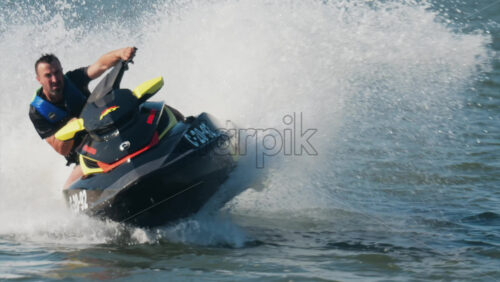 Chisinau, Moldova – June 17, 2025: A man in a black life vest riding a black jet ski at high speed across a calm body of water - Starpik Stock