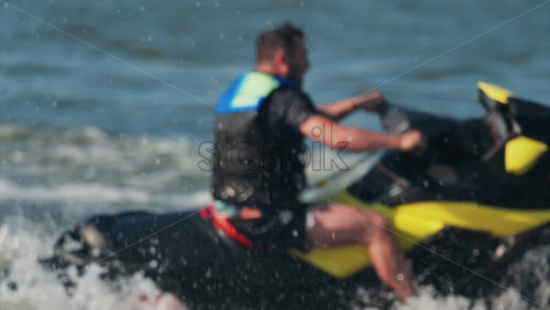 Chisinau, Moldova – June 17, 2025: A man in a black life vest riding a black jet ski at high speed across a calm body of water - Starpik Stock