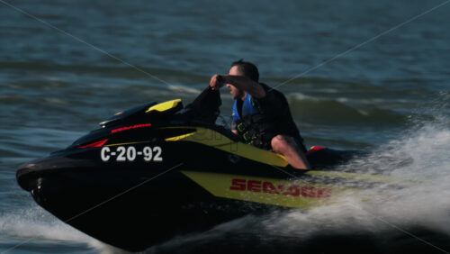 Chisinau, Moldova – June 17, 2025: A man in a black life vest riding a black jet ski at high speed across a calm body of water - Starpik Stock