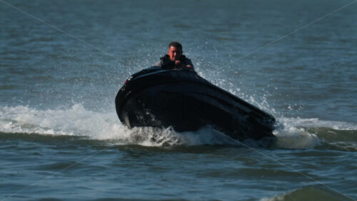 Chisinau, Moldova – June 17, 2025: A man in a black life vest riding a black jet ski at high speed across a calm body of water - Starpik Stock