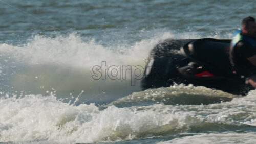 Chisinau, Moldova – June 17, 2025: A man in a black life vest riding a black jet ski at high speed across a calm body of water - Starpik Stock