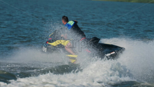 Chisinau, Moldova – June 17, 2025: A man in a black life vest riding a black jet ski at high speed across a calm body of water - Starpik Stock