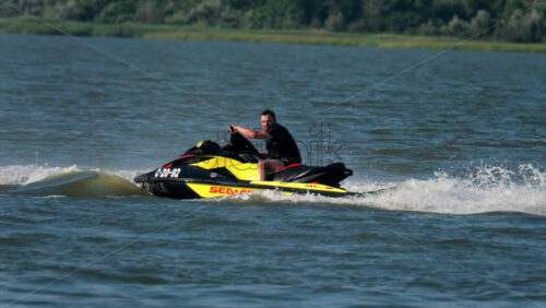 Chisinau, Moldova – June 17, 2025: A man in a black life vest riding a black jet ski at high speed across a calm body of water - Starpik Stock