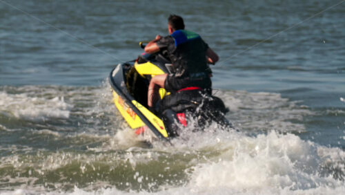 Chisinau, Moldova – June 17, 2025: A man in a black life vest riding a black jet ski at high speed across a calm body of water - Starpik Stock