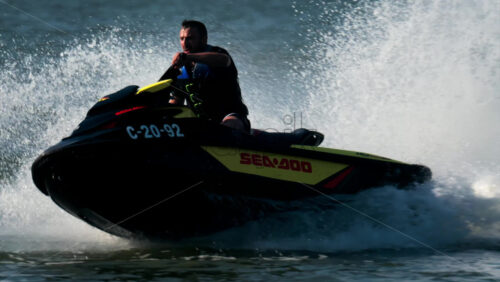 Chisinau, Moldova – June 17, 2025: A man in a black life vest riding a black jet ski at high speed across a calm body of water - Starpik Stock